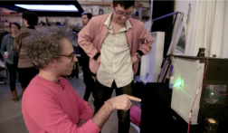 Prof. Graham Jones with student looking at a student project that is a green light glowing spectrally behind a translucent fabric